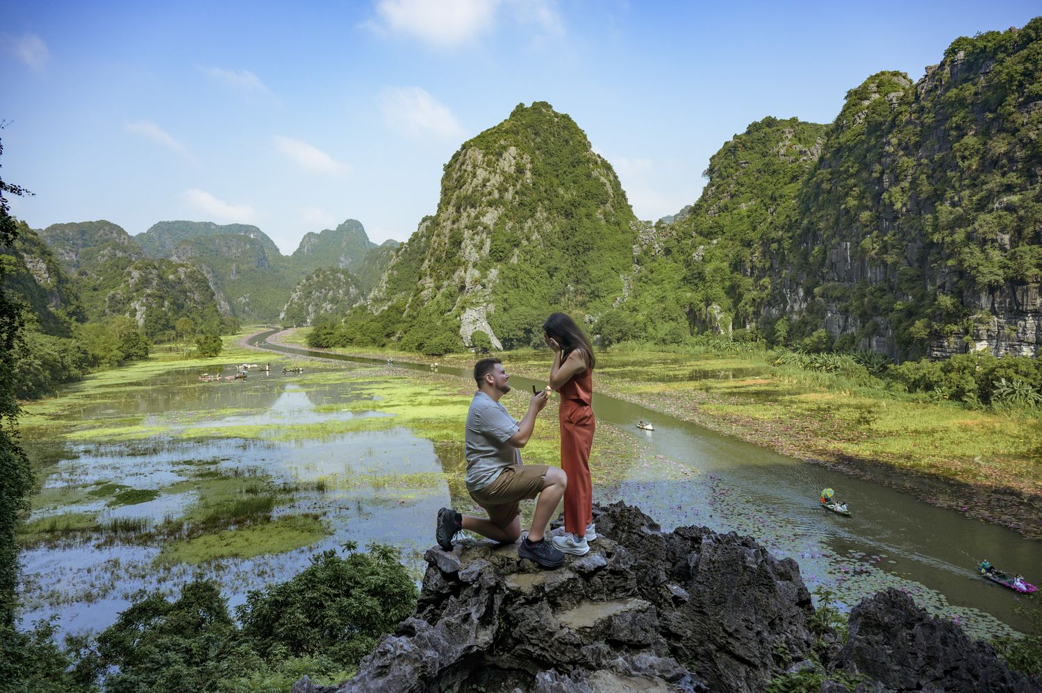 Eric on one knee proposing to Natalie on a rock above the river at Ninh Binh, Vietnam